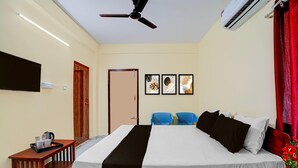 Habitación de hotel con cama, ventilador de techo, aire acondicionado, televisor, una mesita con bandeja y una puerta.