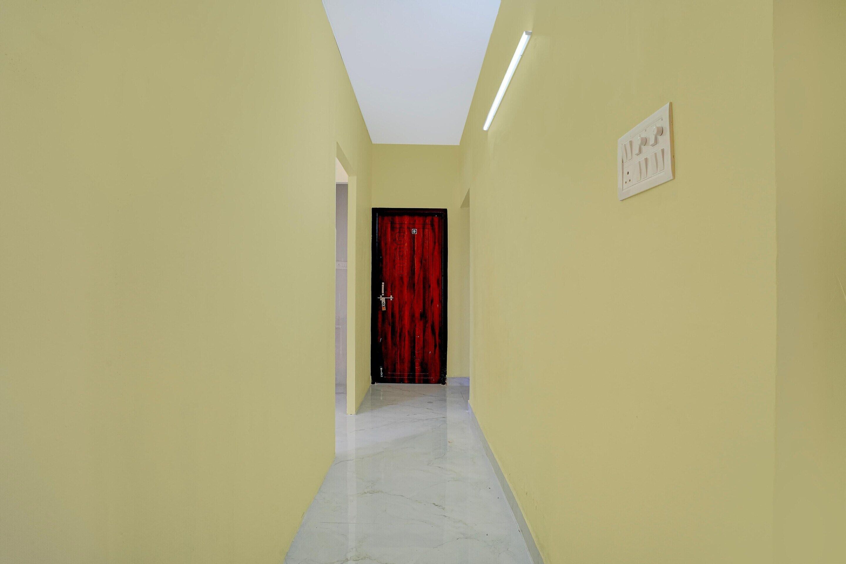 Un couloir étroit aux murs jaunes, une porte rouge au fond, et un luminaire fixé au mur.