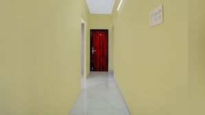 Un pasillo estrecho con paredes amarillas, una puerta roja al final y una lámpara en la pared.