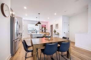 A modern kitchen with a dining area, wooden flooring, and a large clock on the wall. - Luxury Townhouse with Skyline Views & Rooftop BBQ (Indianapolis)