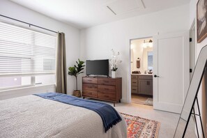 A bedroom with a bed, a dresser, a television, and a bathroom visible through an open door. - Luxury Townhouse with Skyline Views & Rooftop BBQ (Indianapolis)