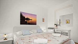 Ein Schlafzimmer mit Bett, Nachttisch, Lampe und einem Sonnenuntergangsbild.