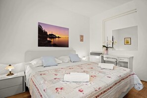 A bedroom with a bed, bedside table, lamp, and a painting of a sunset. - Casa Melita / Apartment with balcony Anina (Rovinj)