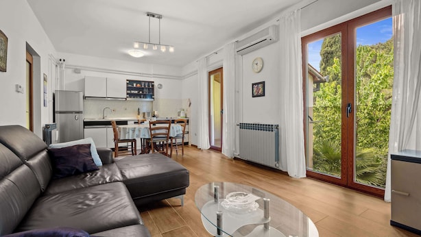 Ein modernes Wohnzimmer mit einer Ledersofa, einem Glastisch und Blick auf eine Küche und einen Garten durch große Schiebetüren.