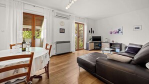 Ein Wohnzimmer mit einer Couch, einem Esstisch mit Stühlen, einem Fernseher und einer Küchenzeile.