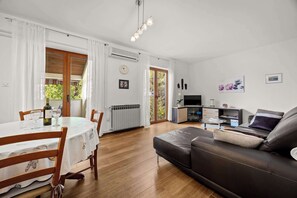 A living room with a sofa, a dining table with chairs, a TV, and a kitchen area. - Casa Melita / Apartment with balcony Anina (Rovinj)