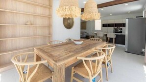 A dining area with a wooden table and chairs, two hanging light fixtures, and a kitchen in the background. - VILLA SEA VIEWS V7 (Amarilla Golf)