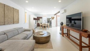 A modern living room with a sofa, a round coffee table, a TV on a wooden stand, and a kitchen in the background. - VILLA SEA VIEWS V7 (Amarilla Golf)