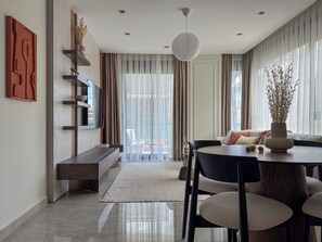 A modern dining area with a round table, chairs, a vase, and a view through large windows. - Qoople Legend D-16 Premium 2-bedroom apartment in Alanya by the sea (Alanya)