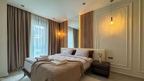 Ett modernt hotellrum med en stor säng, ett nattduksbord, en lampa och utsikt över staden genom fönstret.