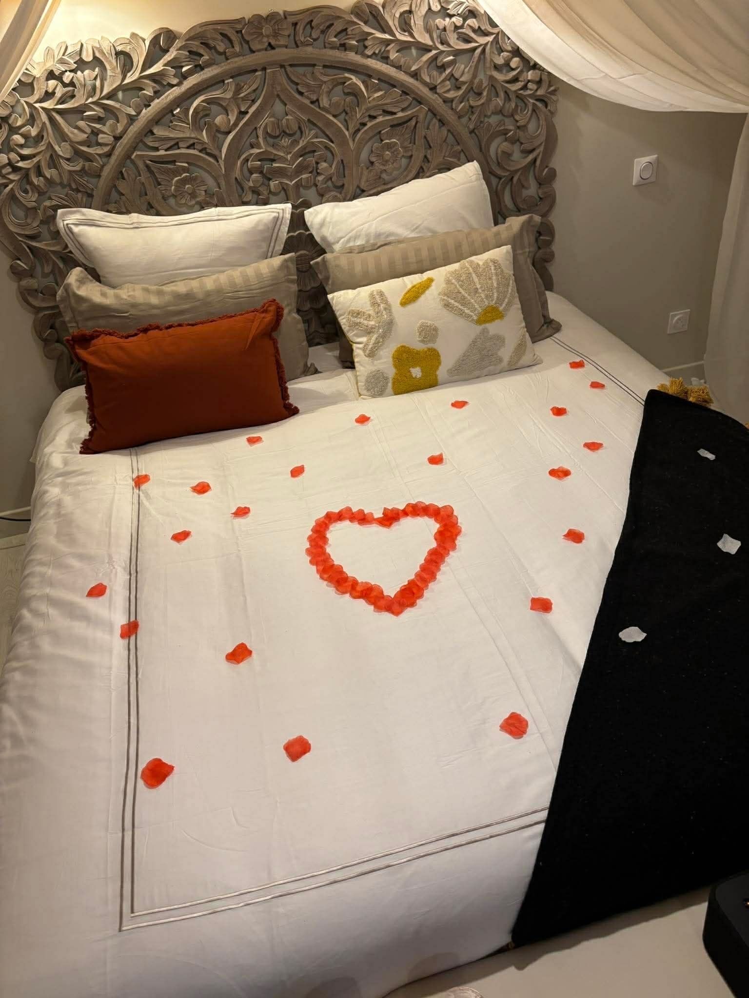 Una cama con decoración en forma de corazón, ropa de cama blanca y varias almohadas.
