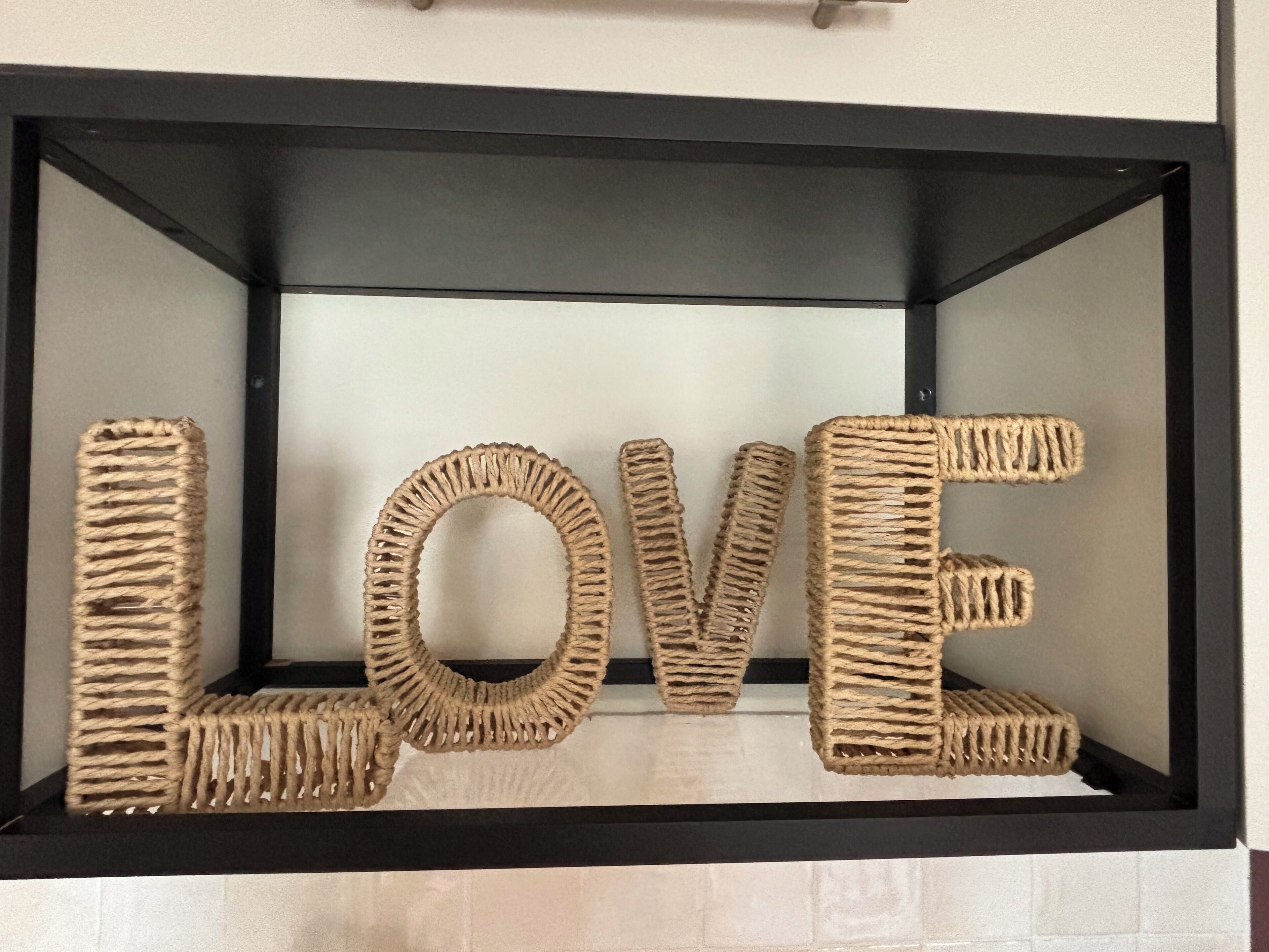 Uma vitrine com moldura preta, com a palavra 'LOVE' escrita em material trançado.