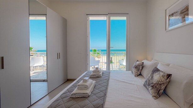 Ein Schlafzimmer mit Bett, Blick auf den Strand und einem Balkon mit Sitzgelegenheiten.