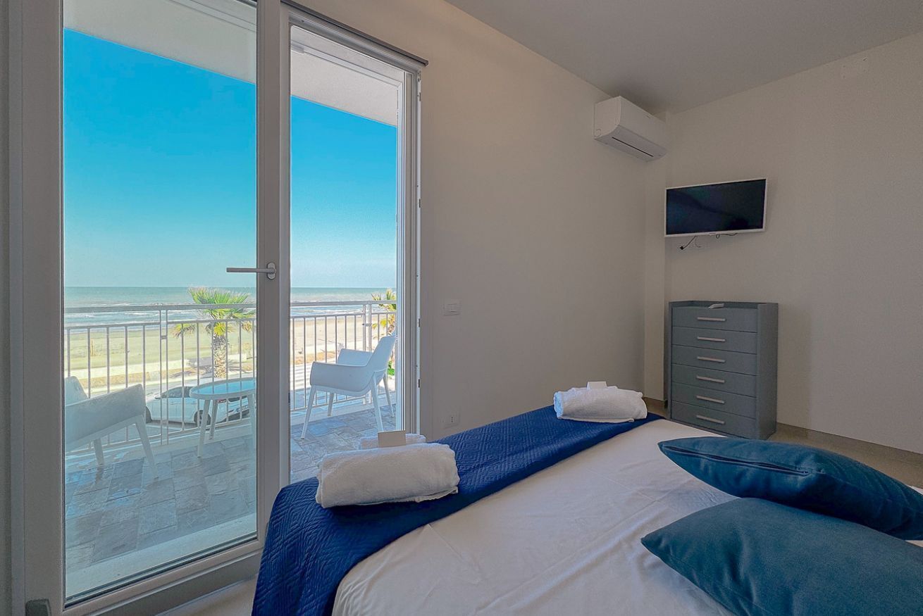 Une chambre avec un lit, une télévision, une armoire et un balcon donnant sur la plage.