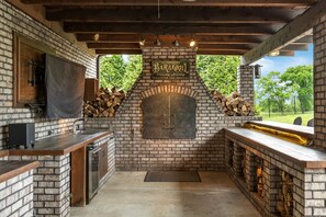 Eine Außenküche mit Kamin aus Ziegelsteinen, einer Bar und einem Grill.