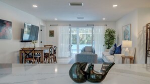 A modern living room with a dining area, a flat-screen TV, and a large window with curtains. - A Perfect Place: Newly Remodeled Ground Level with Pool! (Holmes Beach)