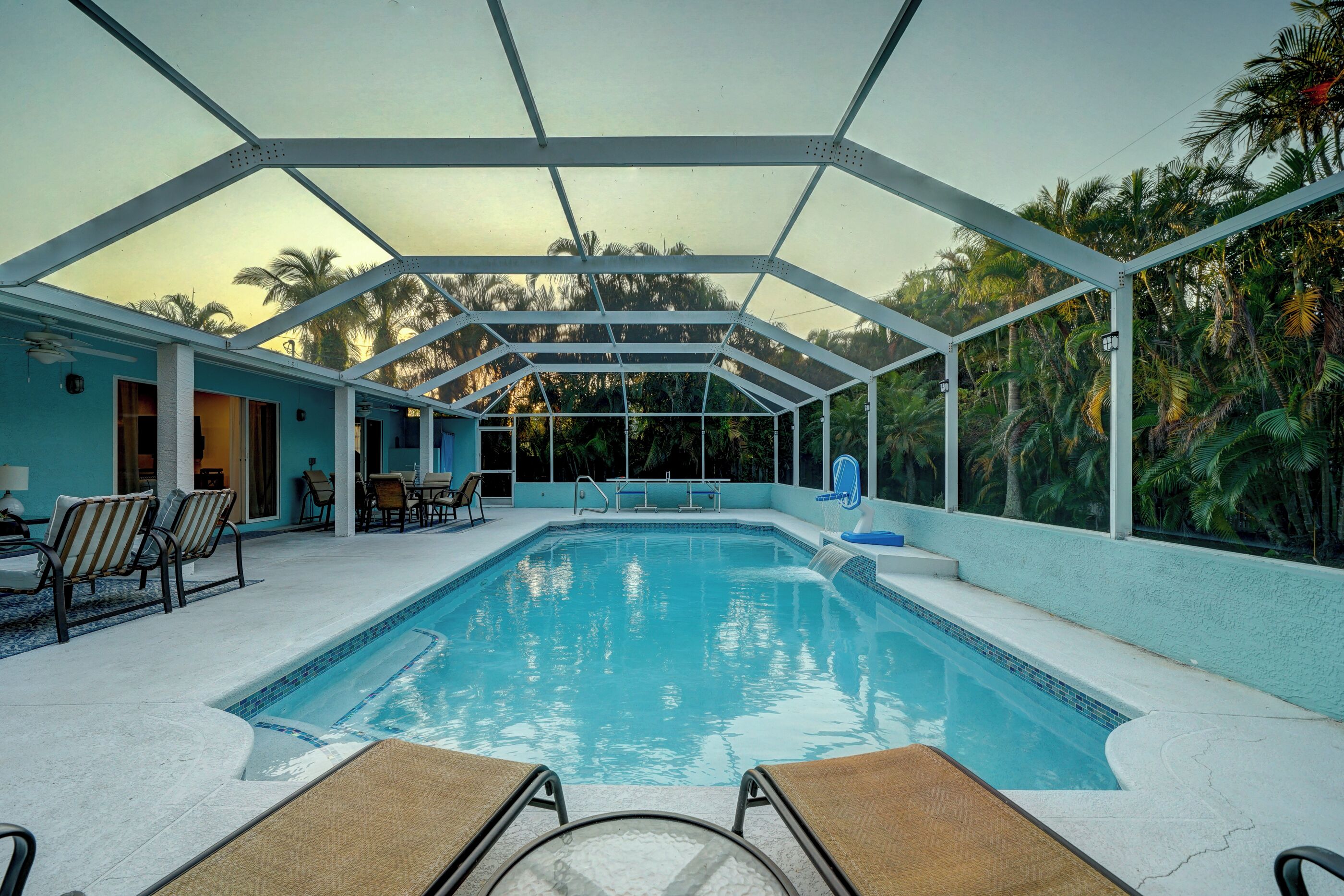 Ein überdachter Pool mit Liegestühlen und Blick auf Palmen.