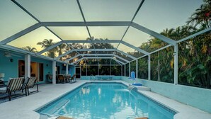 A covered swimming pool with lounge chairs and a view of palm trees. - A Perfect Place: Newly Remodeled Ground Level with Pool! (Holmes Beach)