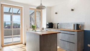 Eine moderne Küche mit einer großen Kochinsel, einer Kaffeemaschine und Blick durch eine Glastür.