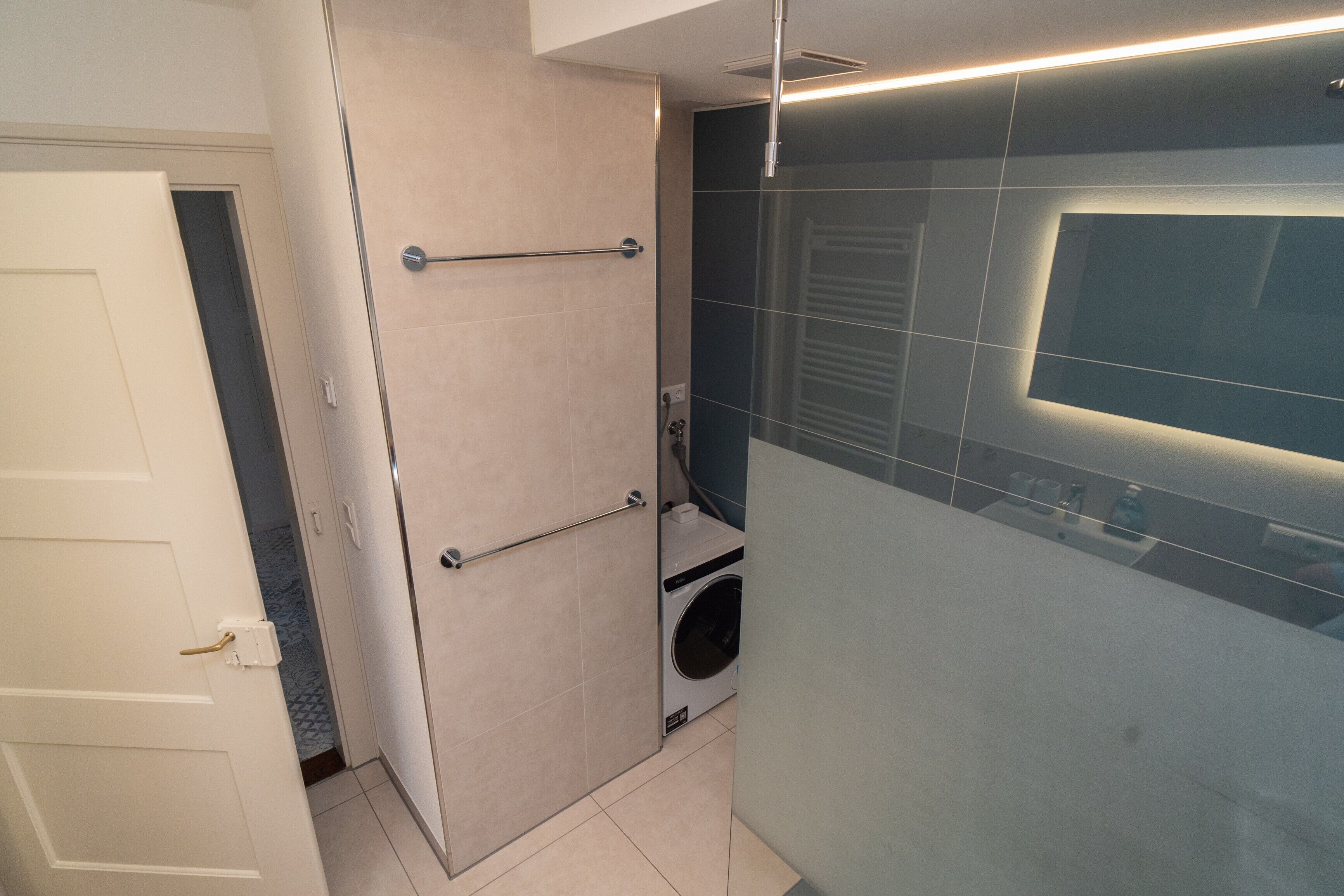Ein modernes Badezimmer mit Duschkabine, integriertem Waschmaschinenanschluss und Handtuchhalter.