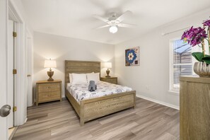 A bedroom with a wooden bed, two bedside tables with lamps, a ceiling fan, a window with blinds, and a wall-mounted artwork. - Private Pool | Gameroom | Value | Near Disney 1162 (Davenport)