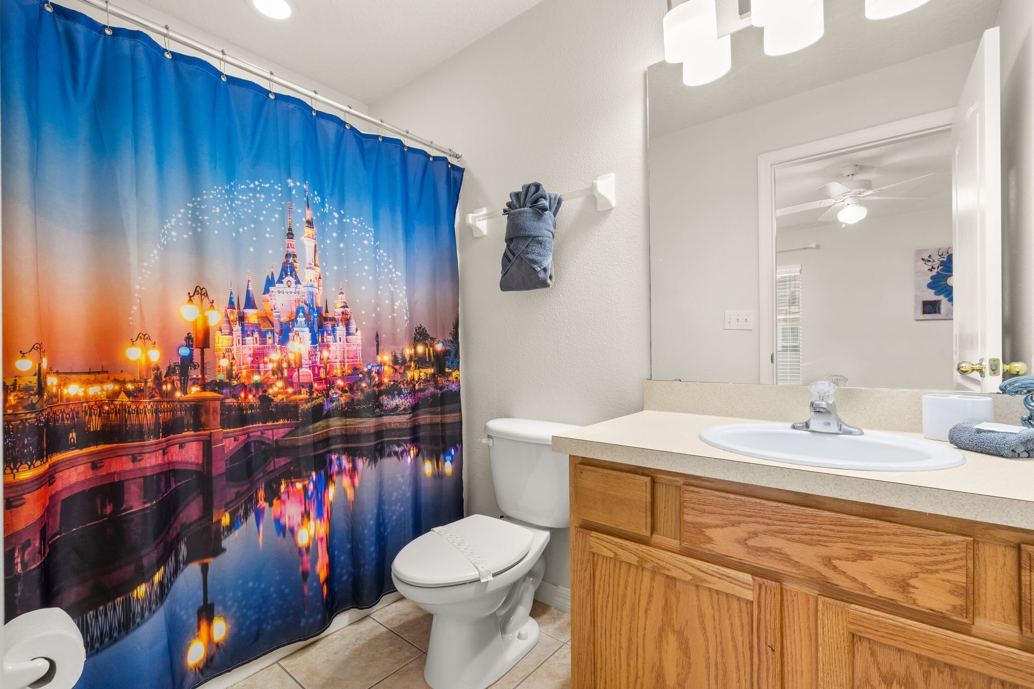 A bathroom with a white toilet, a wooden vanity, a white sink, and a large mirror.