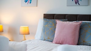 Un lit bien fait, avec une tête de lit, deux lampes de chevet et des coussins décoratifs.