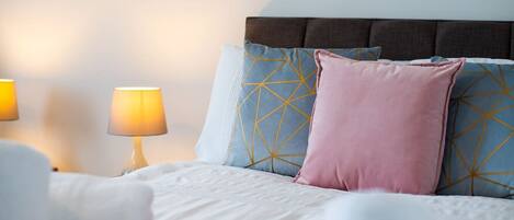 A neatly made bed with a headboard, two bedside lamps, and decorative pillows.