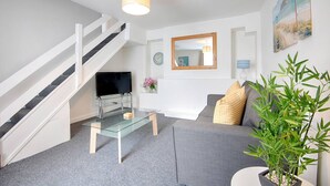 Un salon moderne avec un escalier, un téléviseur à écran plat, une table basse en verre, un canapé et une plante en pot.