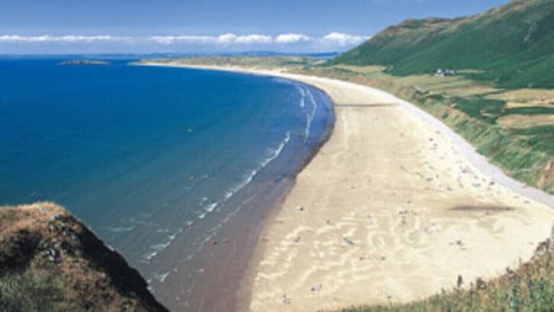 Un paysage côtier avec une plage, l’océan et des collines.