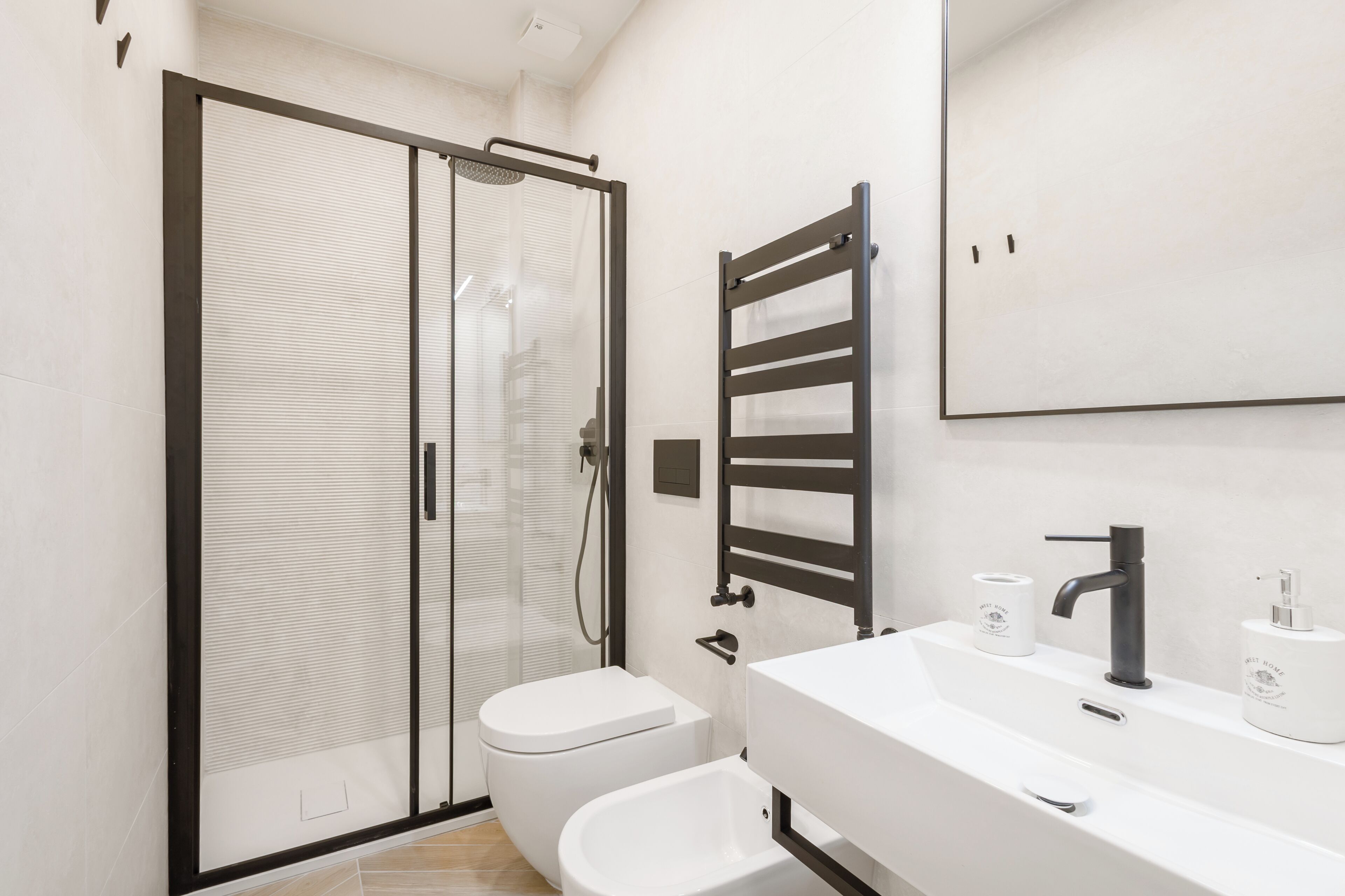 A modern bathroom with a glass shower enclosure, a white toilet, a sink with a black faucet, and a towel rack.