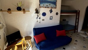 Een knus woongedeelte met een blauwe bank, een klein houten tafeltje, een televisie en een stapelbed.