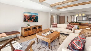 Ein geräumiges Wohnzimmer mit Couch, einer Bank und einem Holztisch, sowie einem großen Gemälde an der Wand.