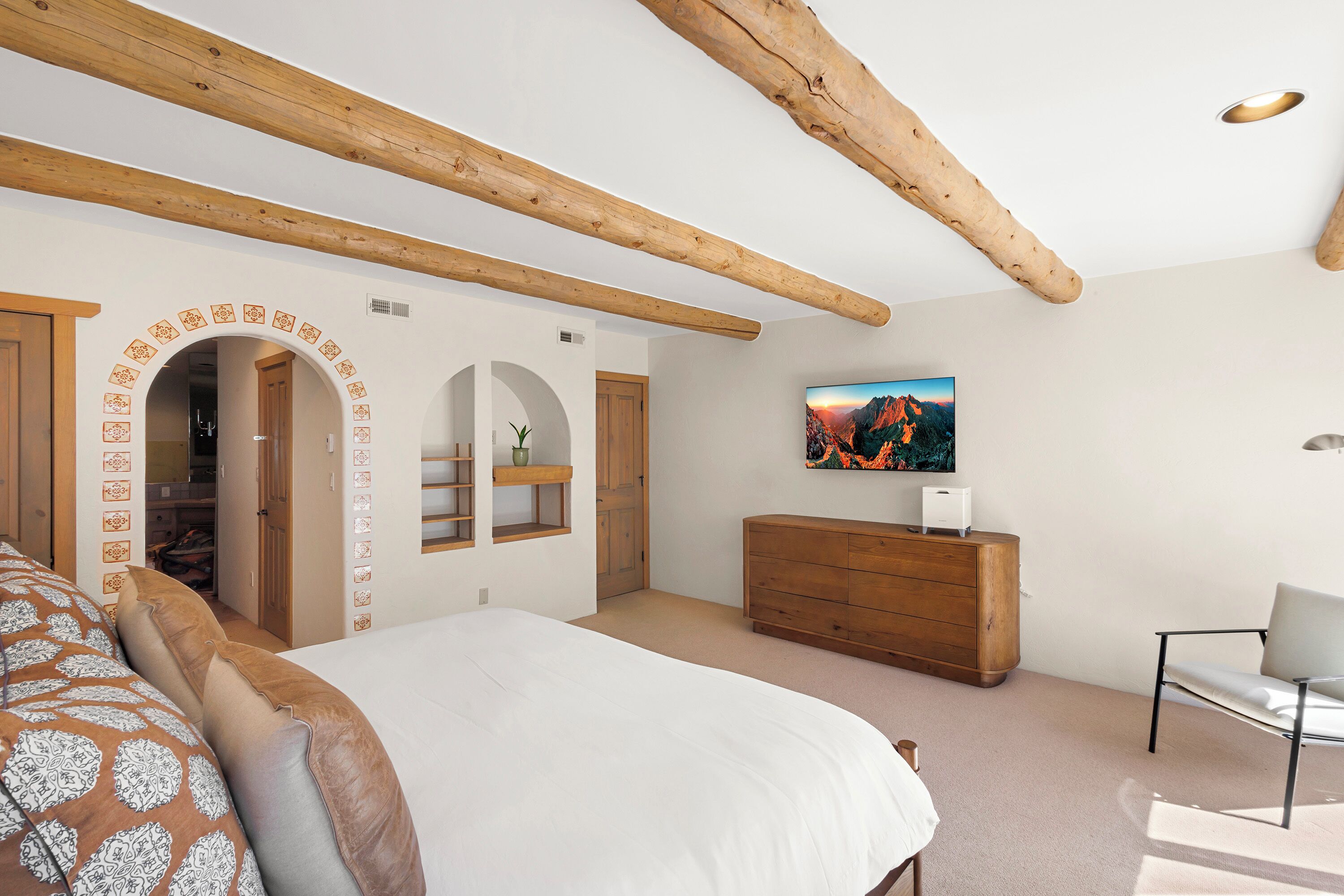 Een slaapkamer met een bed, een houten dressoir, een televisie en een houten balk in het plafond.