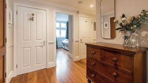 A hallway with wooden flooring, white doors, a dresser with drawers, and a mirror on the wall. - Beautiful apartment in the heart of Mayfair (London)