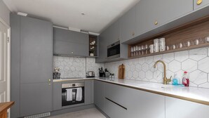 A modern kitchen with grey cabinets, a white countertop, a built-in oven, and a microwave. - Beautiful apartment in the heart of Mayfair (London)