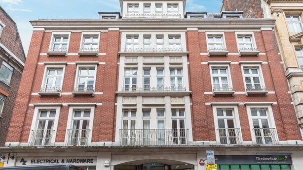 A red brick building with white-framed windows and balconies, a sign for 'Electrical & Hardware,' and a 'Destination Skincare' salon. - Beautiful apartment in the heart of Mayfair (London)