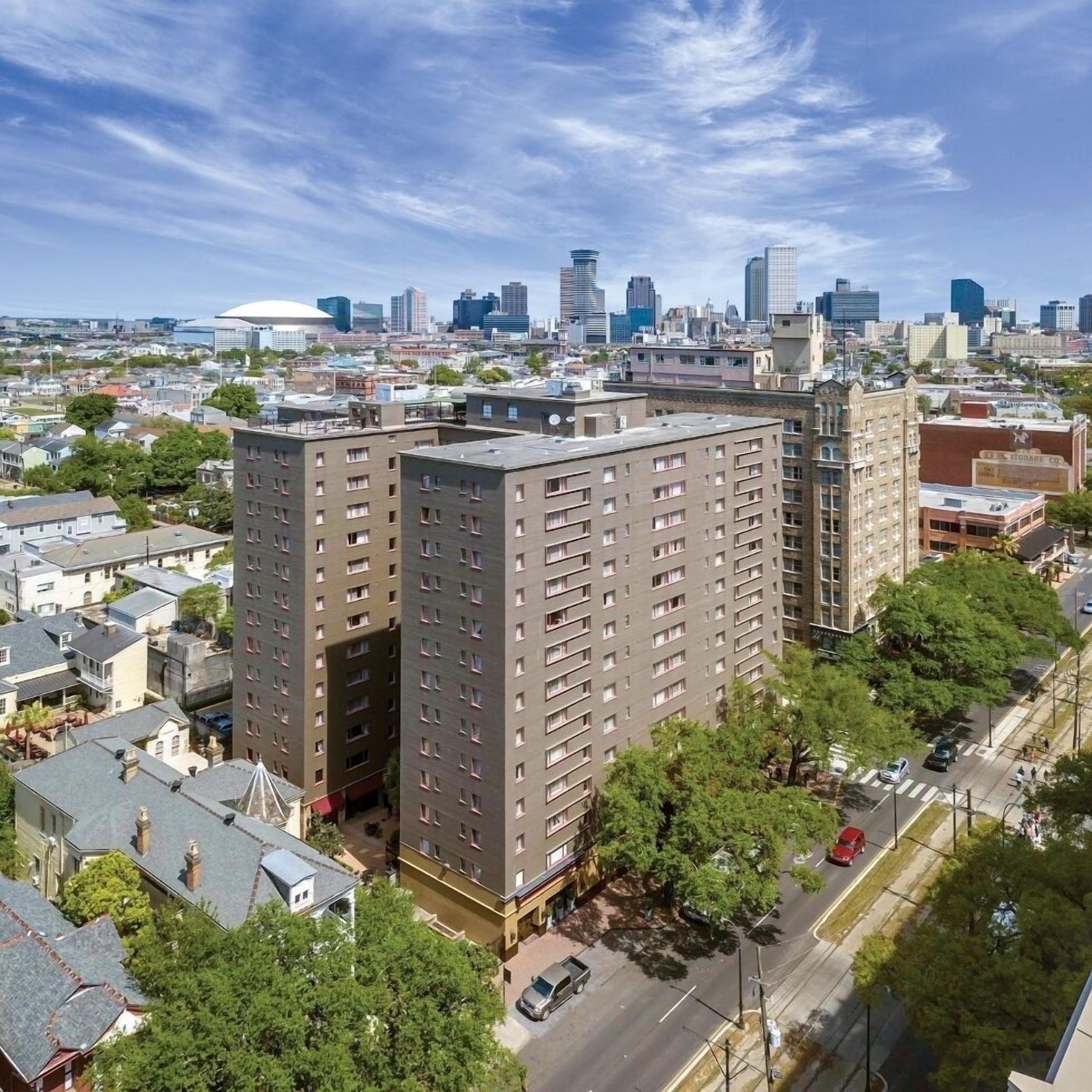 A high-rise building with multiple floors, surrounded by trees and a cityscape in the background.