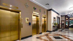A hotel lobby with a marble floor, gold elevators, and a reception desk.