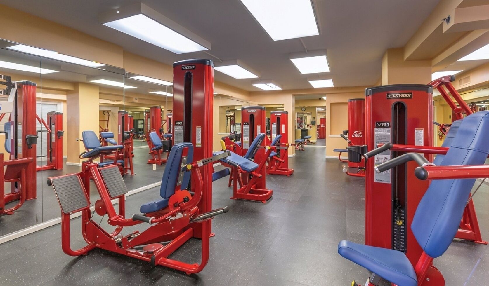 A gym with red and blue exercise equipment, mirrors on the walls, and a clean, well-lit environment.
