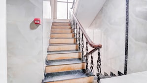 A marble staircase with alternating black and beige steps, a wooden handrail, and a red fire alarm box.