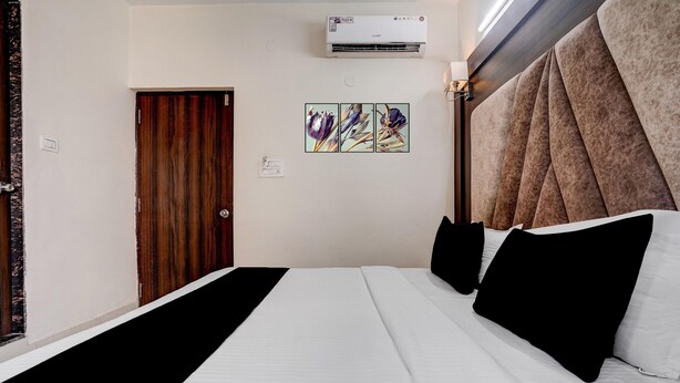 A hotel room with a bed, a wall-mounted air conditioner, a door, and a wall art piece.
