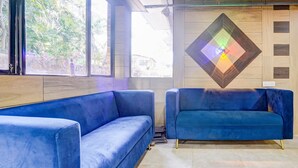 A room with two blue sofas, a wooden wall with a geometric light fixture, and a window with a view of greenery.