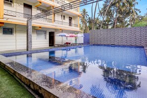 A swimming pool with tiled edges, a covered seating area, and a building with balconies. - Collection O Calangute Circle (Calangute)