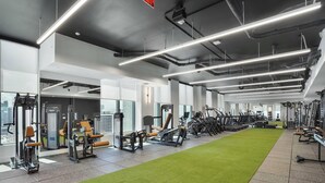 Ein modernes Fitnessstudio mit unterschiedlichen Trainingsgeräten, einem grünen Rasenbereich und großen Fenstern mit Blick auf die Stadt.