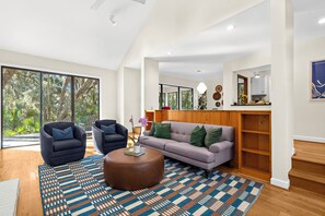 Ein geräumiges Wohnzimmer mit großem Fenster, einer Couch, zwei Sesseln, einem Couchtisch und einem Holzschrank.