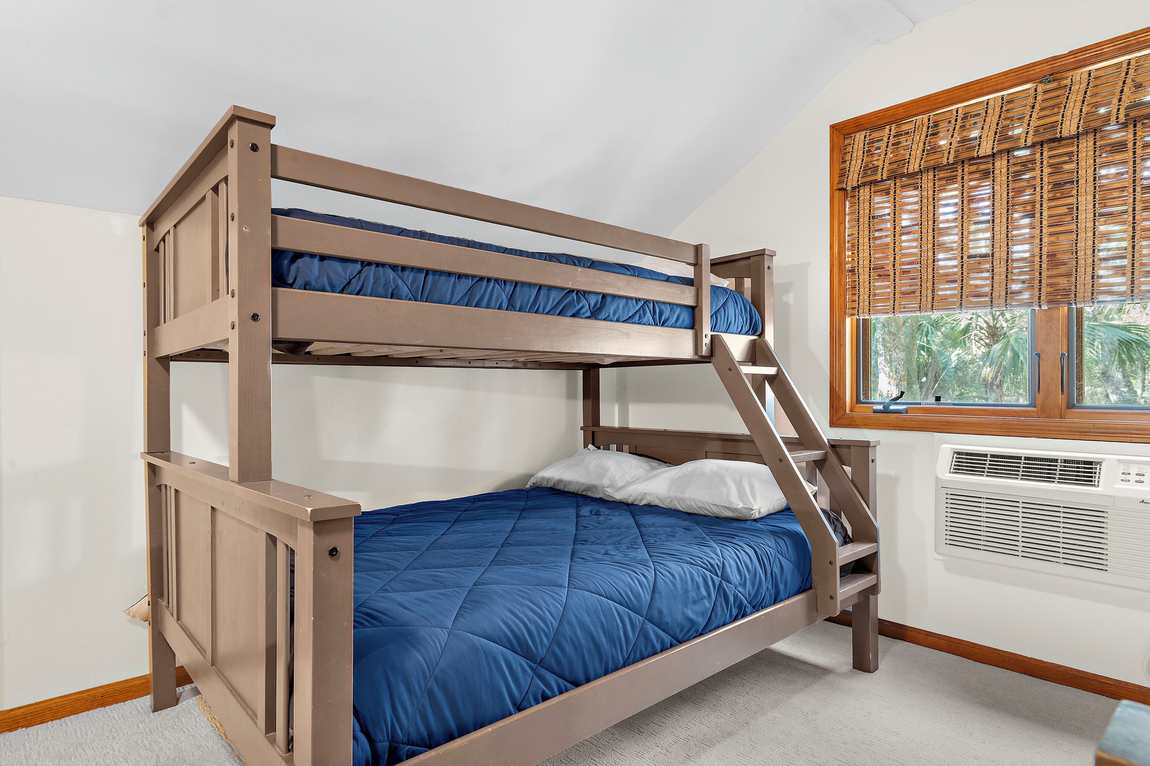 Un lit superposé avec un matelas bleu, une structure en bois et une fenêtre avec des stores.