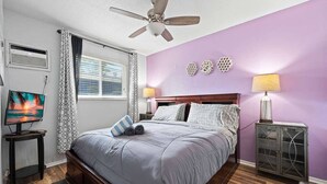 Un dormitorio con cama, ventilador de techo, televisión y elementos decorativos en la pared.