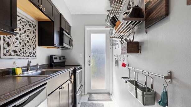 Una cocina con armarios oscuros, un microondas, un lavamanos y una puerta que da a otra habitación.
