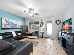 Ein Wohnzimmer mit einer Sofagarnitur, einem Couchtisch, einem Fernseher, einem Deckenventilator und Kunstwerken an den Wänden.